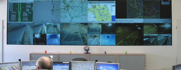 Operator bei der Arbeit. Im Hintergrund eine Multifunktionswand auf der unterschiedliche verkehrstechnische Anlagen angezeigt werden können. Operator bei der Arbeit. Im Hintergrund eine Multifunktionswand auf der unterschiedliche verkehrstechnische Anlagen angezeigt werden können.