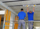 Zwei auf einem Gerüst stehende Bauarbeiter, die auf der Unterseite einer Betondecke Kohlefaserlamellen zur Verstärkung aufkleben