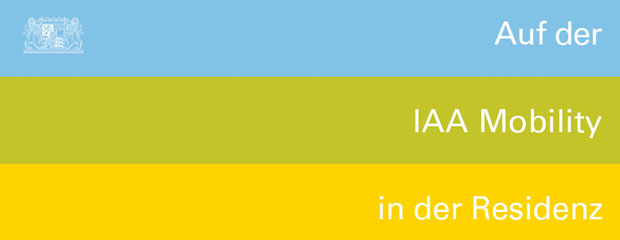 Blauer, grüner und gelber Balken übereinander. In der linken Ecke das kleine Staatswappen. Rechts auf die Balken verteilt der Text "Auf der IAA Mobility in der Residenz" Blauer, grüner und gelber Balken übereinander. In der linken Ecke das kleine Staatswappen. Rechts auf die Balken verteilt der Text "Auf der IAA Mobility in der Residenz"