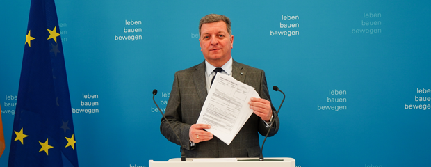 Bauminister Christian Bernreiter steht an einem Rednerpult. Er hält einen mehrseitigen Antrag in den Händen. Bauminister Christian Bernreiter steht an einem Rednerpult. Er hält einen mehrseitigen Antrag in den Händen.
