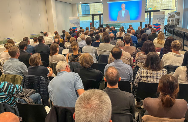 Blick von hinten auf einen vollbesetzten Vortragssaal. Vor dem Publikum eine Leinwand mit Bauminister Christian Bernreiter. Blick von hinten auf einen vollbesetzten Vortragssaal. Vor dem Publikum eine Leinwand mit Bauminister Christian Bernreiter.