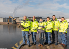 Gruppenbild mit sechs Personen, die eine gelbe Sicherheitsweste tragen. Die Personen halten ein Tau in den Händen. Im Hintergrund ist der Hafen Bamberg zu sehen.