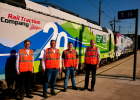 Hier sind 4 Personen mit orangenen Warnwesten vor einem Güterzug zu sehen. 