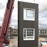 Ein Holzelement eines Hauses wird mit einem Kran auf einer Baustelle richtig platziert. Ein Holzelement eines Hauses wird mit einem Kran auf einer Baustelle richtig platziert.