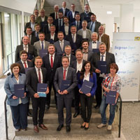 Gruppenfoto mit Verkehrsminister Christian Bernreiter und den Kommunalvertreterinnen und -vertretern für 27 Fahrrad-Projekte der Radoffensive "Klimaland Bayern". Sie stehen auf einer Treppe im Foyer des Bauministeriums . Die Kommunalvertreter halten jeweils eine Urkunde.