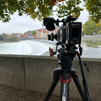 Eine Kamera auf einem Stativ steht an einem Flussufer. Im Hintergrund ist eine Stadt zu sehen. Eine Kamera auf einem Stativ steht an einem Flussufer. Im Hintergrund ist eine Stadt zu sehen.