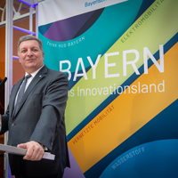Verkehrsminister Christian Bernreiter steht an einem Rednerpult. Im Hintergrund kann man auf einem Roll-up "Bayern - das Innovationsland" lesen. Verkehrsminister Christian Bernreiter steht an einem Rednerpult. Im Hintergrund kann man auf einem Roll-up "Bayern - das Innovationsland" lesen.